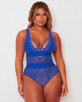 Model wearing the Alicia Fuller Bust Curvy Girl Bodysuit in Bluebird Blue, featuring a plunging neckline with decorative strappy detailing, lace-trimmed cups, sheer mesh panelling, and a sculpting high-waisted silhouette designed for fuller bust support.