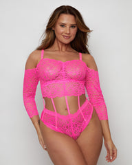 Model wearing the Alix Bodysuit in vibrant Pink, featuring floral lace throughout, an off-the-shoulder neckline, long lace sleeves, and striking cut-out detailing through the waist connected by delicate strap accents.
