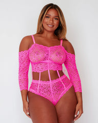 Model wearing the Alix Bodysuit in vibrant Pink, featuring floral lace throughout, an off-the-shoulder neckline, long lace sleeves, and statement cut-out detailing through the waist connected by delicate strap accents.