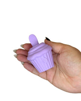 Hand holding a purple silicone cupcake-shaped item against a white background