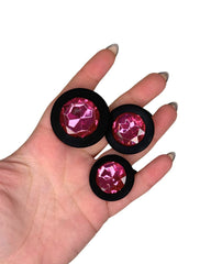 Three pink gemstones in black holders held in a hand against a white background