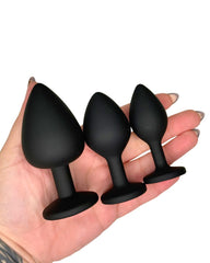 Three black silicone butt plugs held in a hand on a white background