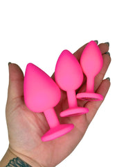 Three pink silicone butt plugs held in a hand against a white background