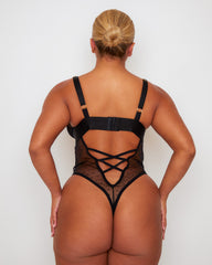 Back view of the Tutti Rouge Stormy Bodysuit in Midnight Black showcasing an open back with lace-up detailing, adjustable straps and sheer mesh thong silhouette.