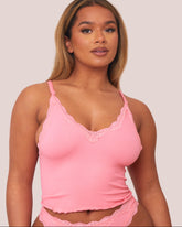 Woman wearing a pink lace-trimmed camisole against a plain background