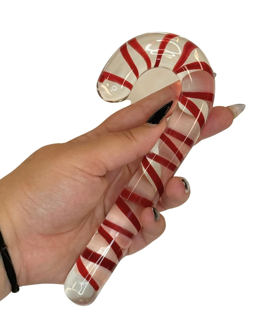 Glass candy cane with red and white stripes held by a hand on a white background