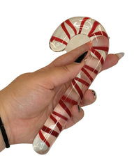 Glass candy cane with red and white stripes held by a hand on a white background