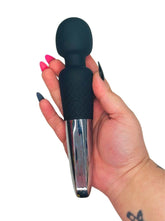Hand holding a black and silver personal massager adult toy against a white background