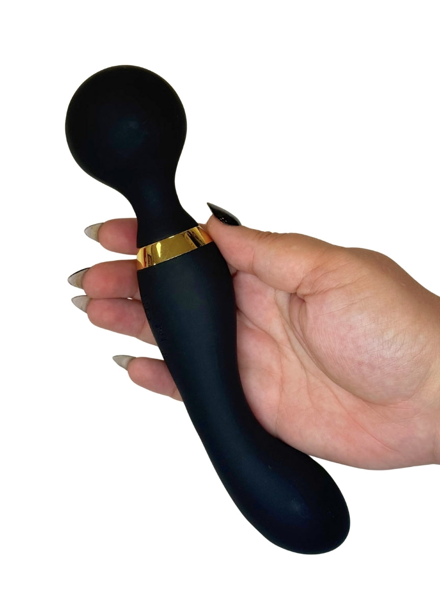 Black handheld massager with gold accent held by a hand on a white background
