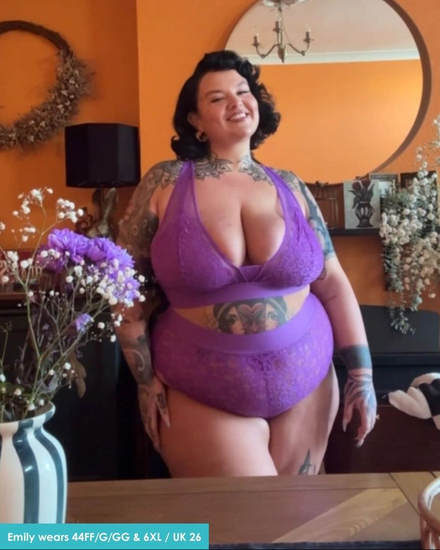 Woman wearing a purple lingerie set in a room with orange walls and decorative elements.
