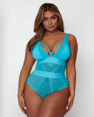 Model wearing the Alicia Fuller Bust Curvy Girl Bodysuit in Bluebird Blue, featuring a plunging neckline with decorative strappy detailing, lace-trimmed cups, sheer mesh panelling, and a sculpting high-waisted silhouette designed to flatter and support fuller busts.