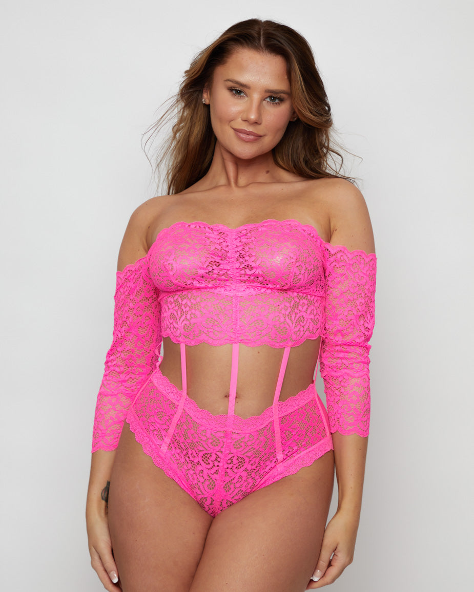 Front view of the Alix Bodysuit in Pink worn with the shoulders exposed, featuring a romantic lace bandeau neckline, long lace sleeves, decorative cut-outs, and high-waisted brief styling.