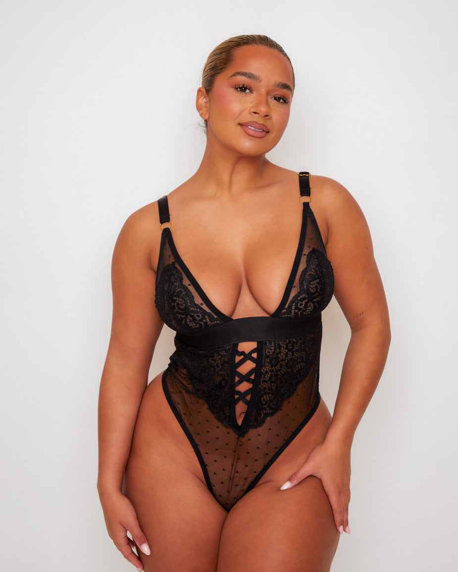 Front view of the Tutti Rouge Stormy Bodysuit in Midnight Black featuring floral lace cups, sheer dotted mesh, plunging neckline, criss-cross front detail and high-leg thong design.