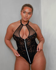 Front view of the Tutti Boudoir Zuri Bodysuit in Onyx Black, featuring a daring halterneck design, plunging fishnet keyhole neckline, floral lace body and statement silver front zip for an unforgettable look.