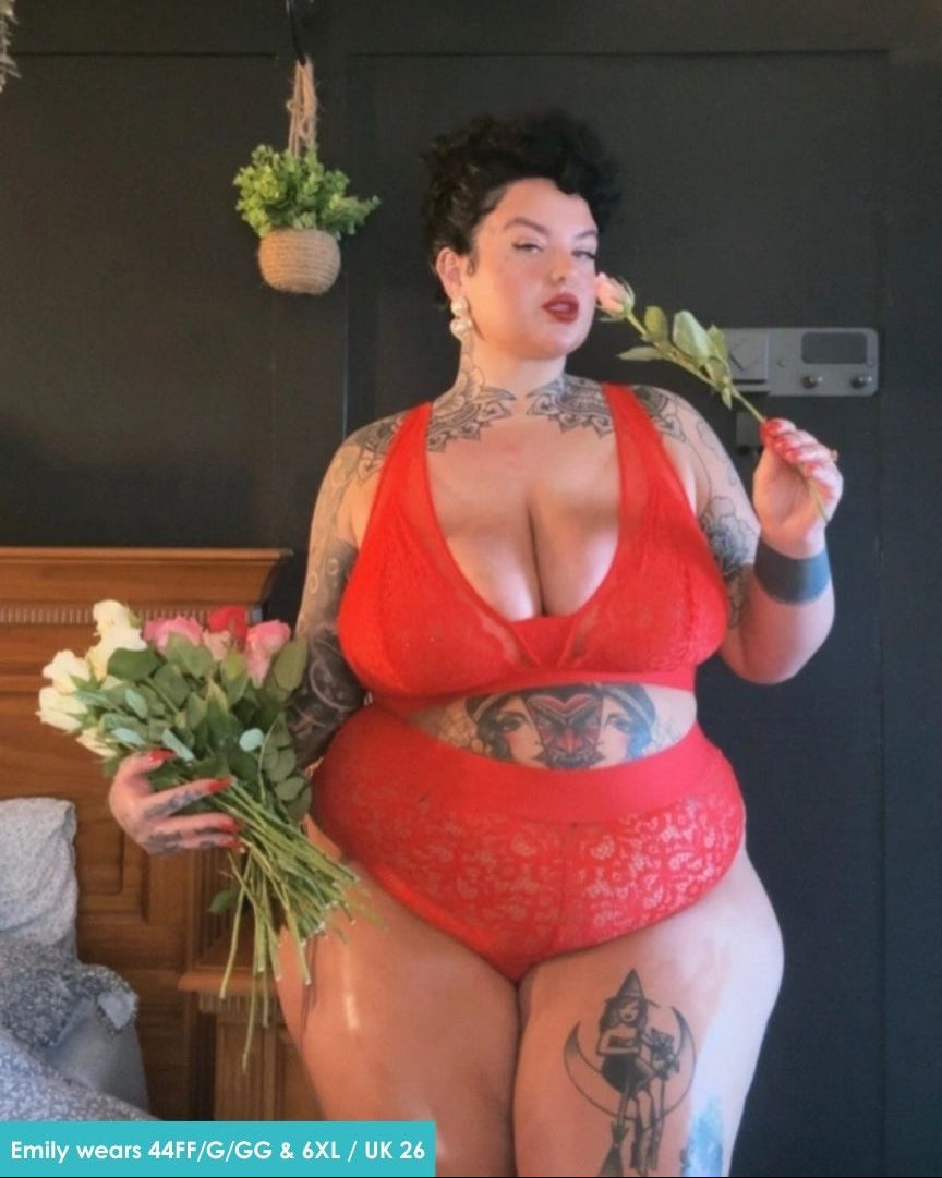 Customer wearing the Hallie Bralette and Brief Set in Chilli Pepper Red from Tutti Rouge, posing indoors while holding flowers. The set features floral lace detailing and a supportive fuller-bust fit.