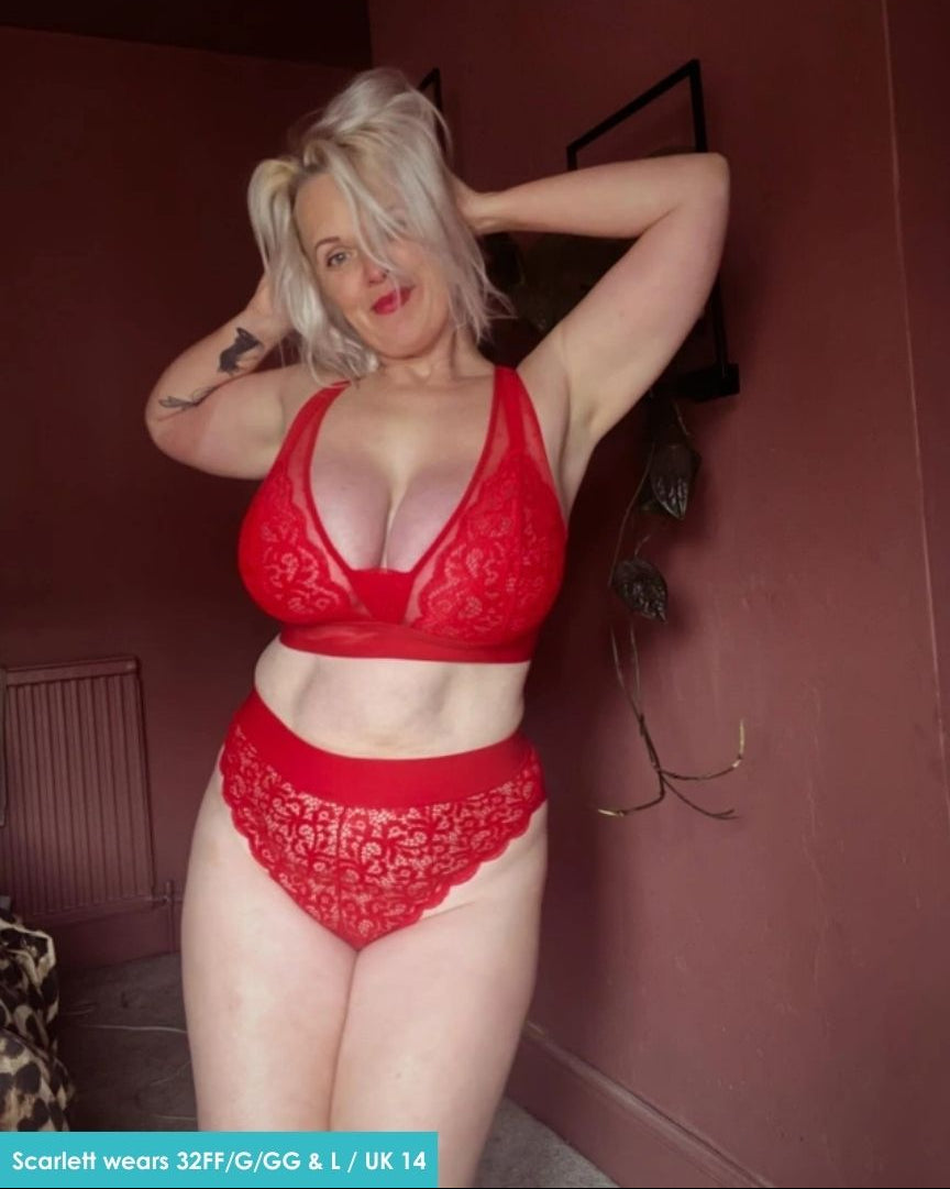 Customer wearing the Hallie Bralette and Brief Set in Chilli Pepper Red from Tutti Rouge, posing in a bathroom. The lace bralette and matching briefs feature sheer mesh accents and a comfortable supportive fit.