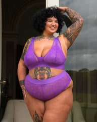 Curvy tattooed model wearing the Hallie Passion Purple lingerie set by Tutti Rouge, posing confidently outside in a sheer lace bralette and matching briefs.